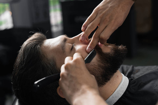 Straight razor cut mans beard in barbershop. Barber man making hairstyle for handsome man - Foto, Imagem