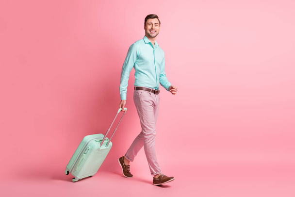Πλήρες μήκος σώματος μέγεθος φωτογραφία του χαρούμενου τουρίστα με αποσκευές σπεύδουν να τερματικό αεροδρόμιο χαμογελώντας απομονωμένο σε παστέλ ροζ χρώμα φόντο - Φωτογραφία, εικόνα
