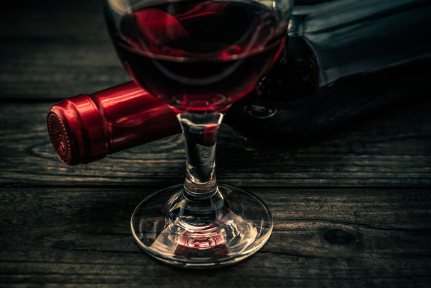 Bottle of red wine with a glass of red wine on an old wooden table - Photo, image