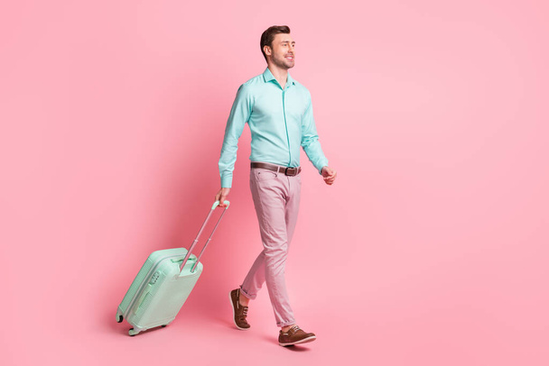 Full length body size photo of happy man with suitcase going to terminal in airport smiling isolated on pastel pink color background - Valokuva, kuva