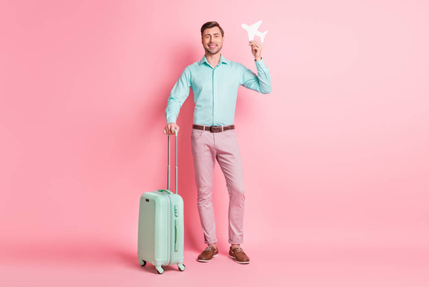 Full length body size photo of young man with luggage keeping airplane figure smiling isolated on pastel pink color background - Foto, Imagem