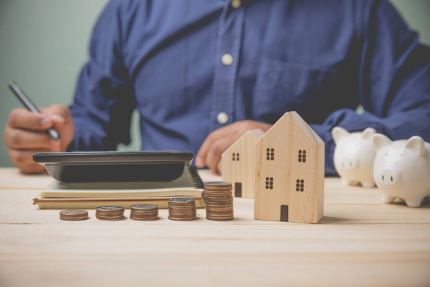Businessman using calculator calculate account for buy house into the future with coins stacking piggy banks and home wood model. Concept accounting, saving money for loan buy house, business. - Foto, Imagen