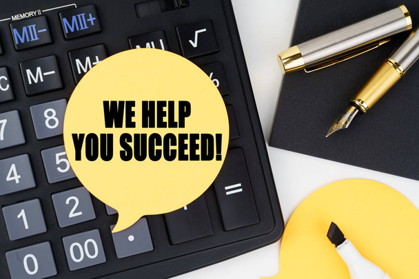 Business and economy concept. There is a calculator, a pen, a marker and a sticker with the inscription - WE HELP YOU SUCCEED - Fotoğraf, Görsel