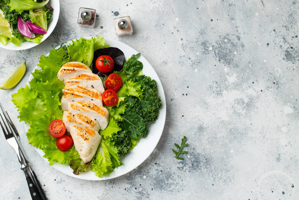 Chicken breast fillet and vegetable salad with tomatoes and green leaves on a light background. The concept of healthy food and keto diet. Top view with copy space. - Foto, Bild