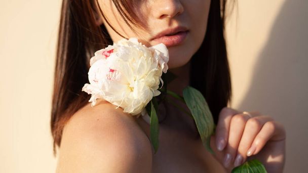 a menina segura em sua mão uma flor branca tocando o ombro perto dos lábios. o conceito de beleza natural - Foto, Imagem