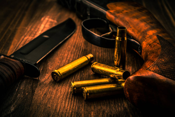 Prázdné náboje s puškou a bojovým nožem ležící na dřevěném stole - Fotografie, Obrázek