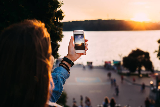 The girl keeps her mobile phone and takes pictures of the sunset - Photo, Image