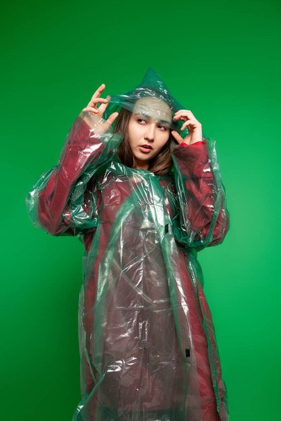 Woman in raincoat standing in studio on green background - Фото, зображення