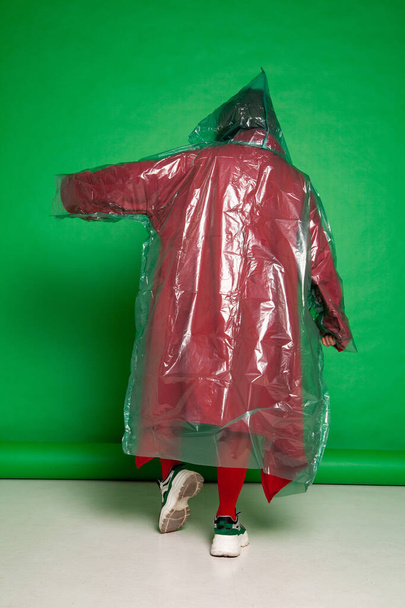 Unrecognizable woman in raincoat in studio on green background - Fotó, kép