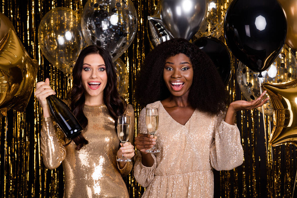 Photo of tow amazed festive ladies hold glasses champagne bottle party isolated on shine glitter bright background - Photo, Image