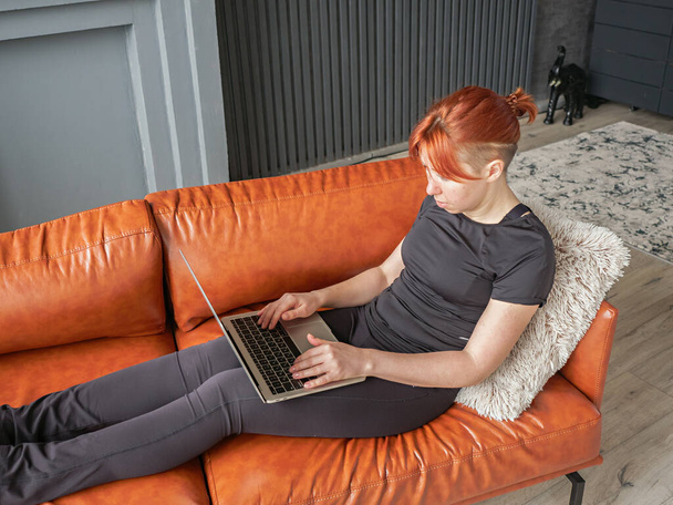 Young woman typing on laptop sitting on sofa in home interior. Top down close up view to girl working at home. Concept of female business online. - Foto, Bild