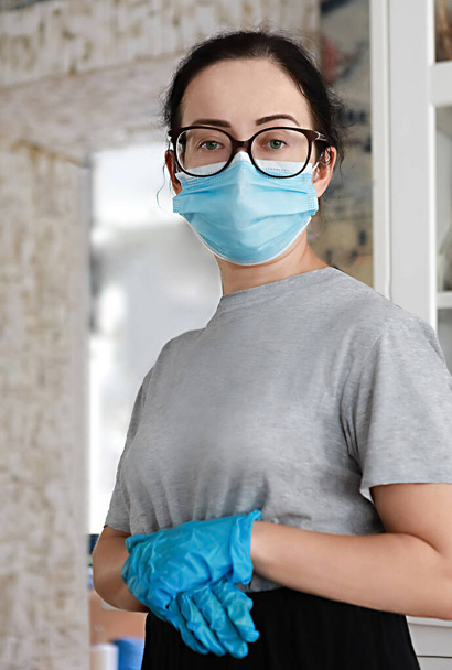 Surullinen nuori nainen, jolla on suojaava naamio, lasit ja lääketieteelliset käsineet, on itsekäs kotona Covid 19 koronavirus pandemian aikana. Soita kaikille Pysy kotona, häviä - Valokuva, kuva