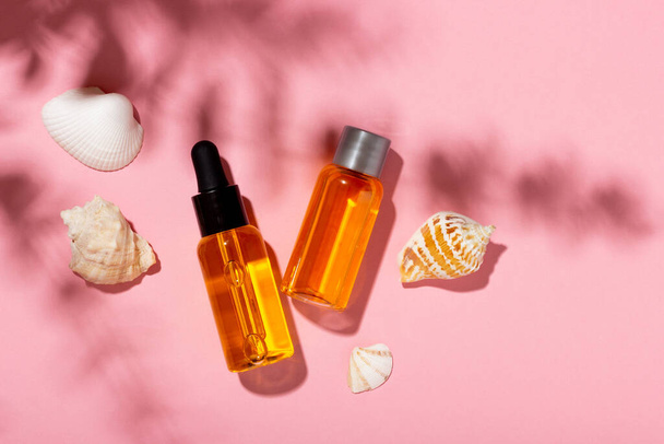 Tanning oil. Cosmetic products next to seashells in sunbeams on a pink background. Sun protective cosmetics. - Foto, Bild