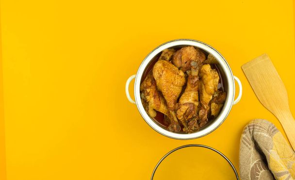 Geroosterde kip in een pan, gebakken kippenpoten voor het avondeten, keuken werkruimte concept, plat lag oranje kleurrijke achtergrond met kopieerruimte, bovenaanzicht foto - Foto, afbeelding