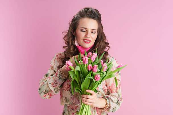 young 40 years old woman with long wavy brunette hair with tulips bouquet and pink mask against pink background. - Foto, immagini