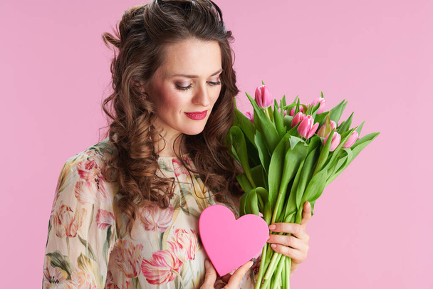 relaxed elegant woman with long wavy brunette hair with tulips bouquet and pink heart isolated on pink background. - Zdjęcie, obraz