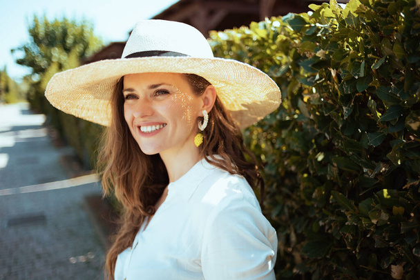 happy elegant woman in white shirt with hat outdoors near green wall. - Fotó, kép