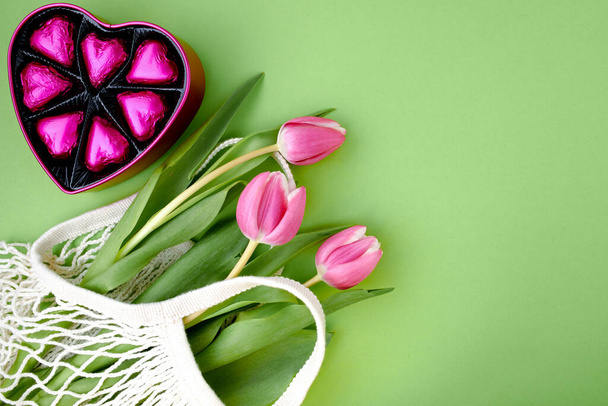 spring flat lay with string bag, heart shaped candy box and tulips isolated on green background. - 写真・画像
