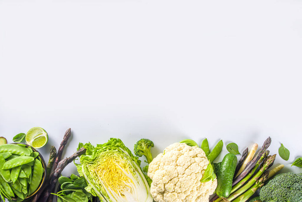 Gezonde voeding Voorjaar voedsel achtergrond. Assortiment van verse rauwe biologische groene groenten - broccoli, bloemkool, courgette, komkommers, asperges, spinazie, avocado, kool op witte achtergrond - Foto, afbeelding