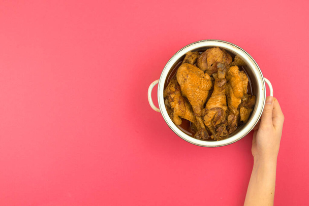Mulher apresentando comida assada de frango para um jantar de família, espaço de trabalho cozinha minimalista e plano de fundo rosa leigos, panela na mão, vista superior e espaço de cópia - Foto, Imagem