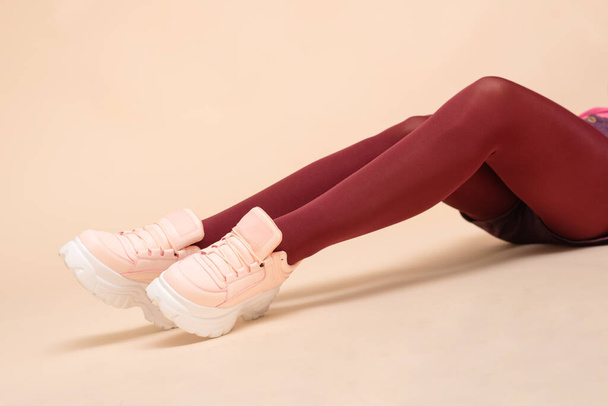 Modern sneakers on the women feet in red stockings close up. - Фото, зображення