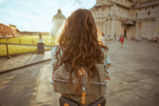 Seen from behind modern woman in floral dress with backpack having walking tour near Cattedrale di Pisa. - Fotó, kép
