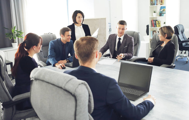 Ομάδα νέων επιτυχημένων δικηγόρων επιχειρηματιών που επικοινωνούν μεταξύ τους σε μια αίθουσα συνεδριάσεων, ενώ εργάζονται σε ένα έργο.  - Φωτογραφία, εικόνα