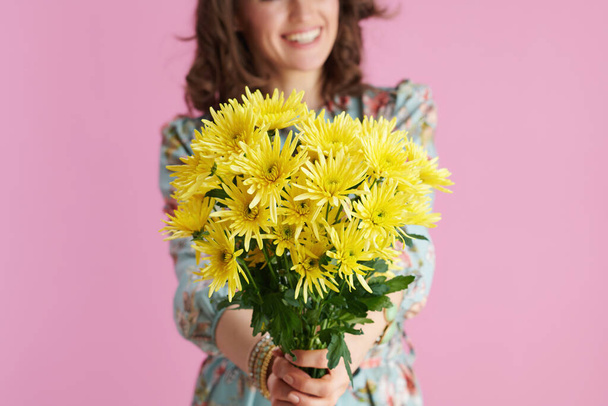 Close-up na mulher feliz de meia-idade com cabelos longos e ondulados morena dando flores amarelas crisântemos contra fundo rosa. - Foto, Imagem