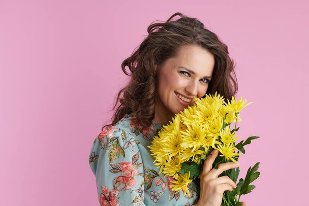 happy stylish woman in floral dress with yellow chrysanthemums flowers against pink background. - Foto, Bild