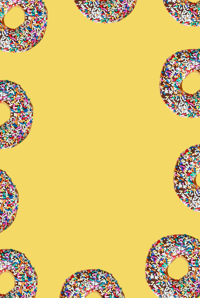 Marco de rosquillas vidriadas de chocolate con espolvoreos de colores sobre fondo amarillo - Foto, imagen
