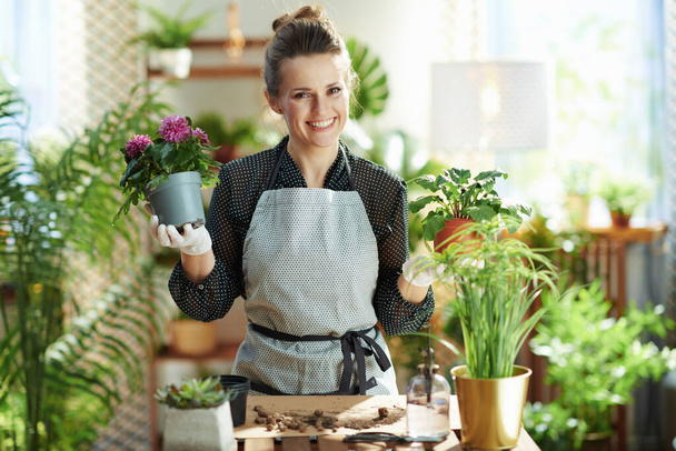 Green home. Portrait of happy modern florist in white rubber gloves with potted plant at modern home in sunny day. - Foto, Imagem