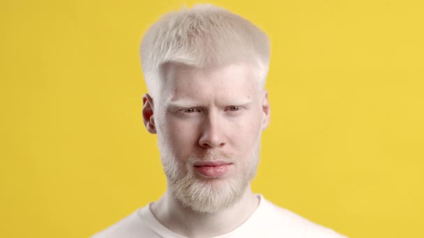 Poważny człowiek albinos pozowanie patrząc na aparat fotograficzny na żółtym tle - Materiał filmowy, wideo