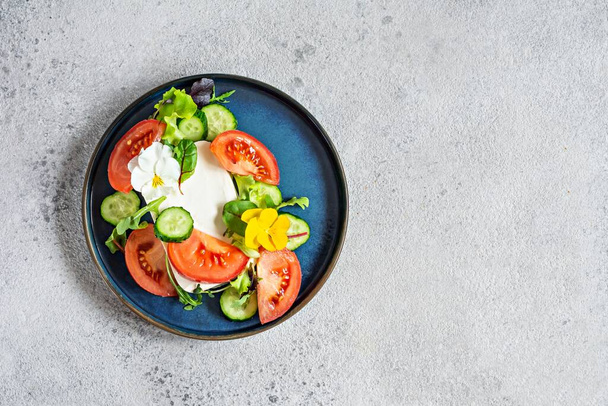 Eetsalade met feta kaas, verse groenten (tomaten, komkommers, uien), krokante sla, microgreens en violette bloemen. Niet-standaard serveren van Griekse salade. - Foto, afbeelding
