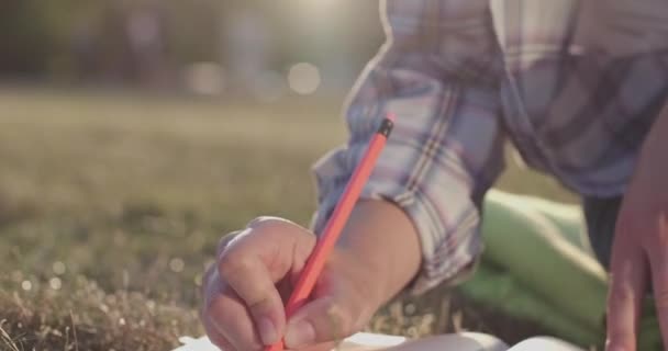 Estudiante hace la tarea de escribir en el cuaderno en el prado exuberante - Imágenes, Vídeo