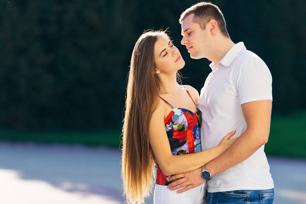 концепция любви, отношений, семьи и людей - пара объятий в летнем парке, мужчина целует женщину. - Фото, изображение