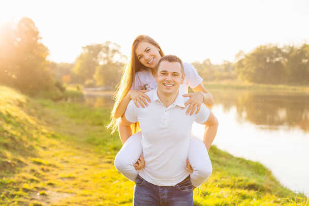 Happy couple in love on a walk on a beautiful summer day. Stylish beautiful girl with a guy having fun together in nature, a man holding a woman on his back. - Photo, Image