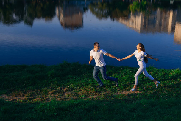 A young man and a girl are walking in the forest by the lake. Happy couple holding hands, running around, having fun. - Foto, Imagem