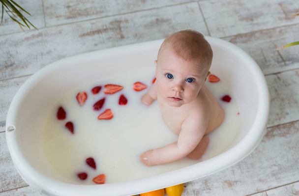 hermoso bebé niño se sienta en un baño de leche con fresas sobre un fondo de madera con espacio para el texto. Fondo de verano - Foto, imagen