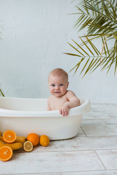 retrato de un pequeño niño desnudo sentado en una bañera y bañándose sobre un fondo blanco con espacio para el texto - Foto, Imagen