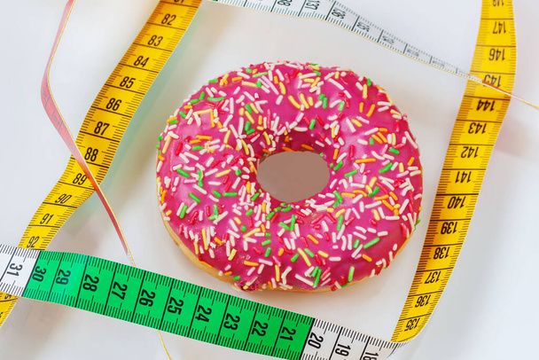 Bright glazed donut and tape measure. Concept of healthy food, lifestyle, diet, overweight - Photo, Image