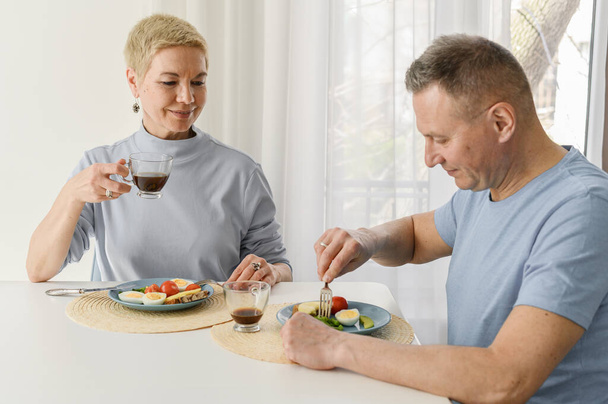 Gesunde reife Paare essen zusammen zu Mittag, sitzen auf dem Tisch, trinken Kaffee und lächeln - Foto, Bild