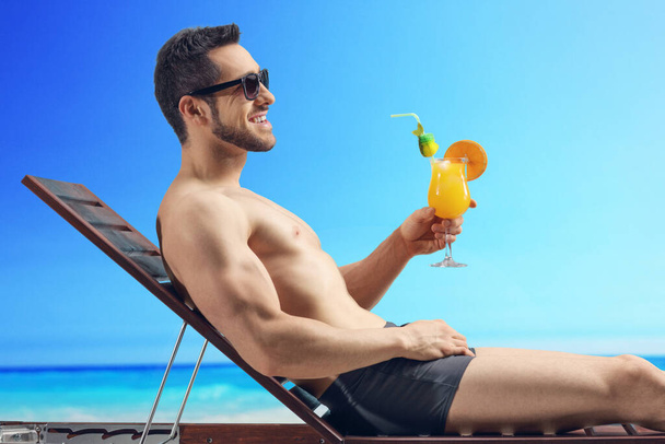 Mies ottaa aurinkoa ja pitää cocktailia meren rannalla - Valokuva, kuva