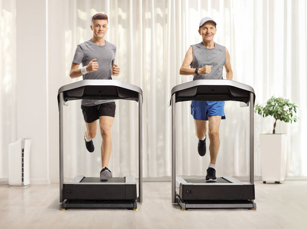 Full length portrait of a young and elderly man running on treadmills in a room with a curtain - Fotoğraf, Görsel
