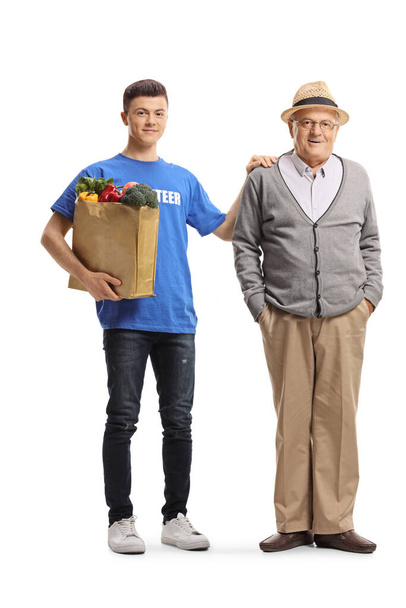 Young male volunteer holding a grocery bag and standing next to elderly man isolated on white background - Photo, Image