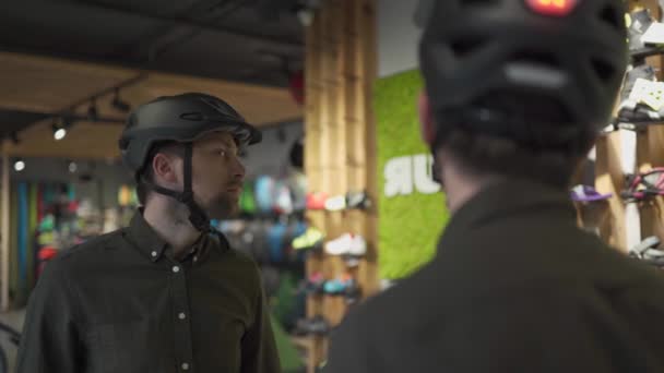 Мужчина осматривает велосипедные шлемы в спортивном магазине, глядя на себя в зеркало. Пробую новый спортивный шлем в магазине велосипедов. Мужчина надевает велосипедный шлем в магазине. Клиент в магазине велосипедов примеряет велосипедный шлем - Кадры, видео