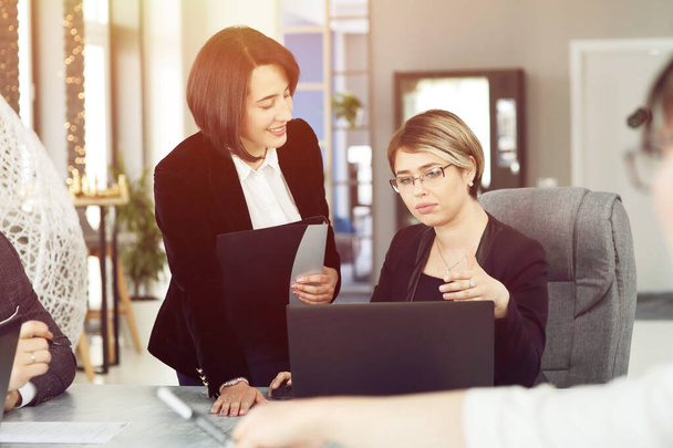 Zwei junge Geschäftsfrauen im Büro, die Informationen analysieren, in einen Laptop schauen und lächeln.  - Foto, Bild