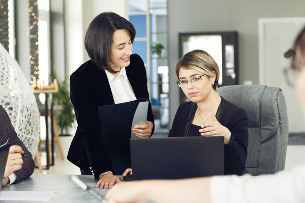 Duas mulheres de negócios jovens no escritório, analisando informações olhando para um laptop, e sorrindo.  - Foto, Imagem