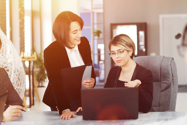 Две молодые деловые женщины в офисе, анализируя информацию, глядя в ноутбук, и улыбаясь.  - Фото, изображение