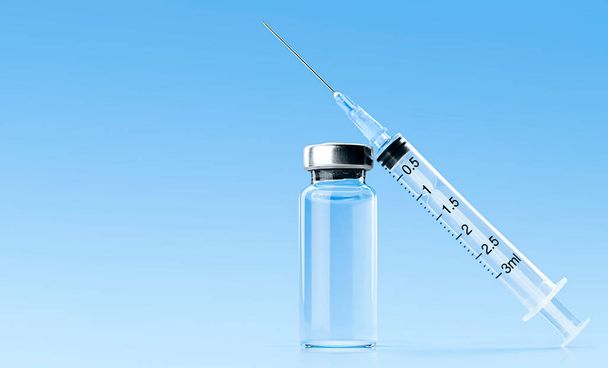 fles en spuit met vaccin op een lichtblauwe achtergrond - Foto, afbeelding