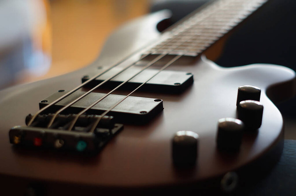 Closeup shot of a smooth body, pickups, bridge, knobs and strings of a bass guitar musical instrument with backlight - Photo, Image